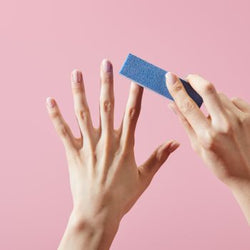 Pulido manual de uñas naturales con un bloque pulidor de uñas azul de 4 caras sobre un fondo rosa